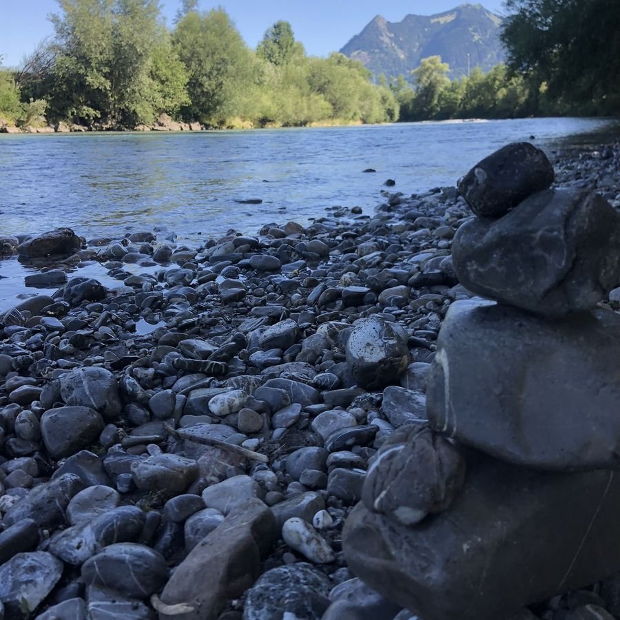 Ein Steinturm am Flussufer, im Hintergrund Berge